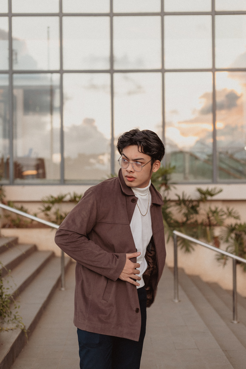 a person wearing glasses and a brown jacket standing in front of a building